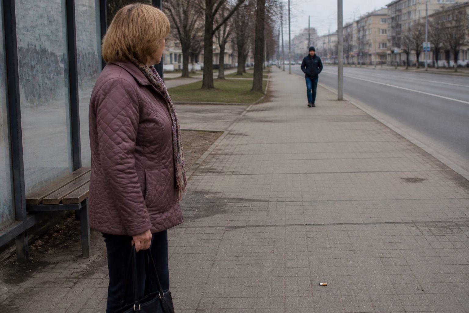 Жінка на зупинці з подивом дивиться на чоловіка, що наближається, поруч недопалок